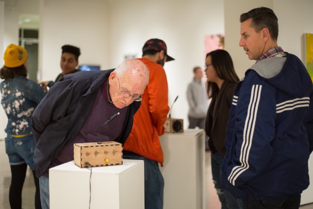 Museumgoers interacting with a Sonic Mirror instrument on a pedestal.