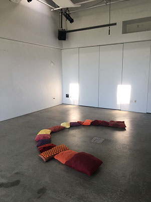 Photo of the Sonic Mirror room installation showing many floor pillows arranged in a semi-circle for audience seating during performances.