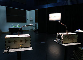Two Sonic Mirror (v2.0) hardware instruments facing each other atop illuminated display pedestals.
