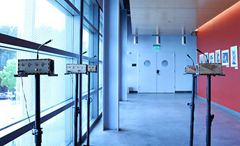 Five Sonic Mirror hardware instruments on speaker stand pedestals in an empty hallway.