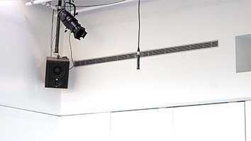 Microphone suspended from ceiling next to a speaker within a large whitebox gallery and multimedia venue.