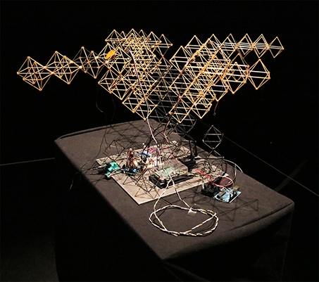 Photo of the complete soft robot and Sonic Mirror acoustic testing system on a lit pedestal at the ultraSHIFT MFA exhibition.