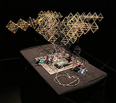 Photo of the complete soft robot and Sonic Mirror acoustic testing system on a lit pedestal at the ultraSHIFT MFA exhibition.